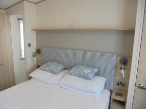 a bed with two blue pillows on top of it at Kingfisher Windermere 6 Berth, Enclosed veranda, Close to site shop in Ingoldmells