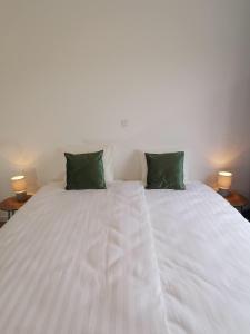 a white bed with two green pillows on it at Ten Velde - vakantiewoning 12 personen - sauna - bubbelbad in Hoeselt