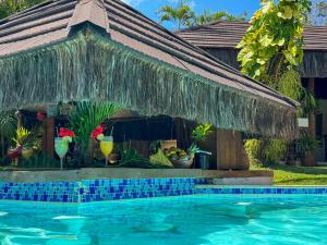 a swimming pool in front of a house with a thatch roof at Pousada Berro do Jeguy in Pipa