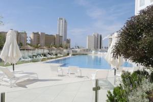 a swimming pool with white chairs and umbrellas at Beach front luxury apartment - managed building in H̱adera