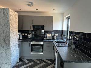 a kitchen with white cabinets and black tiles at Newark House Premium Apartments by DH ApartHotels in Peterborough