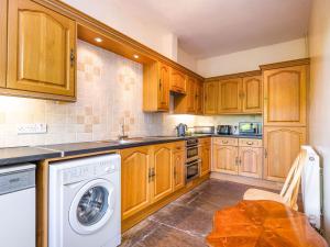 cocina con armarios de madera, lavadora y secadora en The Carthouse, en Hereford