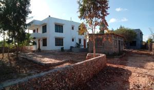 a white house with a wall and a tree at Gemini Villas in Kijiwetanga