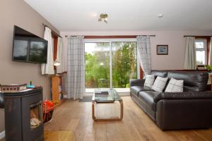 a living room with a black leather couch and a tv at Birch Cottage in Blairmore