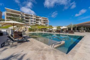 a swimming pool with chairs and umbrellas in front of a building at Spacious New 3BR Condo at Tramonti plus Resort Access in Cabo San Lucas