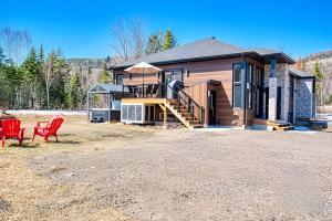 a home with two red chairs and a house at Cottage Quebec - Olivine in Petite-Rivière-Saint-François