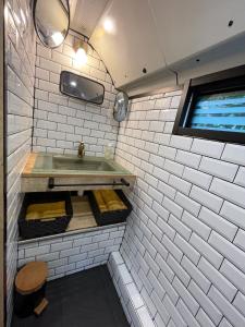 ein Badezimmer mit einem Waschbecken und einer weiß gefliesten Wand in der Unterkunft TERMINUSBUS in Crèvecoeur-le-Grand