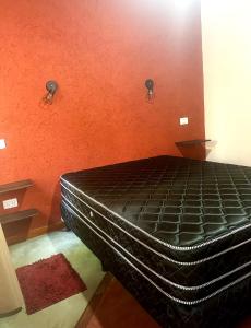 Cama negra en habitación con pared de color naranja en Casa bela energia en Villa Las Rosas