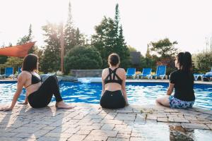 grupa trzech kobiet siedzących wokół basenu w obiekcie Le Cerf #40 w mieście Mille-Isles