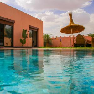 a swimming pool with an umbrella and a building at Hotel Jnane riad in Marrakech
