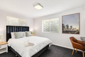 a white bedroom with a bed and a desk and two windows at So Central, So Comfortable! in Toowoomba