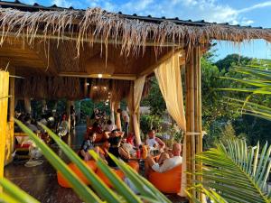 卡塔海灘的住宿－Greenheart garden View Camp phuket，一群人坐在稻草屋顶下的橙色椅子上