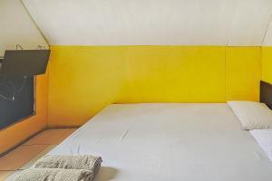 um pequeno quarto com uma cama e uma parede amarela em Cigadog Residence Mitra Reddoorz em Ciwidey