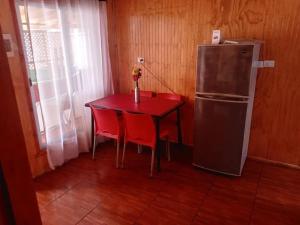 a red table with two red chairs and a refrigerator at Cabañas maule in Coronel