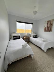 a white bedroom with two beds and a window at Wait and Sea Bargara in Bargara