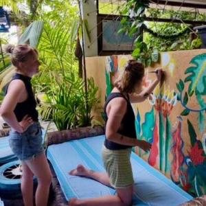 two women are painting a mural on a mattress at Cycling Backpacker Hostel in Unawatuna