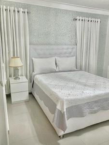 a white bedroom with a bed and a lamp at Acojedor Apartamento in La Francia