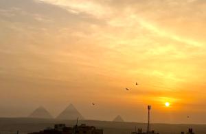 a group of birds flying over the pyramids at sunset at Panorama 3 Pyramids View Inn in Giza