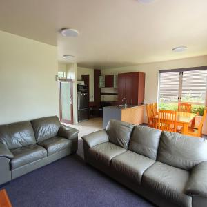 a living room with a leather couch and a kitchen at Kuituna on the Canal Villa, 3 bedrooms in Rotorua