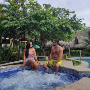 a man and a woman sitting in a swimming pool at Montañita Cabañas in Montañita