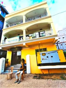 duas pessoas sentadas num banco em frente a um edifício amarelo em Hotel Krishna Residency Puri Excellent Stay em Puri