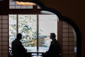 zwei Personen, die an einem Tisch sitzen und aus dem Fenster schauen in der Unterkunft Shoraiso in Yamanouchi