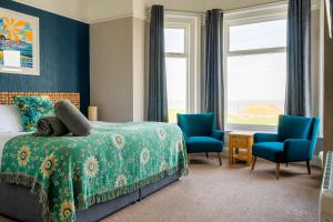 a bedroom with a bed and two blue chairs at Sandcliff Guest House in Cromer