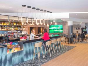 two people sitting at a bar in a restaurant at Novotel Marne-la-Vallée Noisy-le-Grand in Noisy-le-Grand