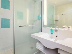 een witte badkamer met een wastafel en een douche bij Novotel Marne-la-Vallée Noisy-le-Grand in Noisy-le-Grand