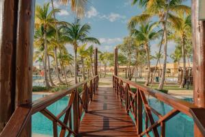 Sports Illustrated Resorts Marina and Villas Cap Cana - All-Inclusive في بونتا كانا: وجود جسر خشبي فوق مسبح في منتجع به أشجار نخيل