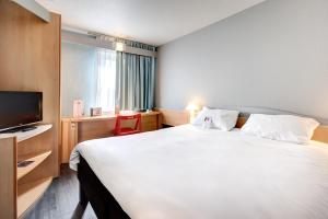 a hotel room with a large white bed and a tv at Ibis Agen Centre Gare in Agen