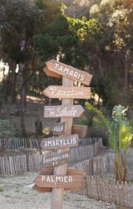 a wooden directional sign in a garden with names at Le Domaine de la mer - Appartements de plage dans un cadre enchanteur in Hyères