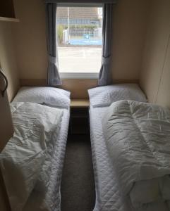 twee bedden in een kleine kamer met een raam bij 6 Berth Caravan With Decking At Naze Marine Holiday Park Ref 17071p in Walton-on-the-Naze