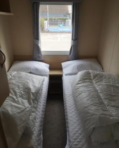 two beds in a small room with a window at 6 Berth Caravan With Decking At Naze Marine Holiday Park Ref 17071p in Walton-on-the-Naze