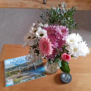 a vase of flowers on a table next to a book at Henblas Holiday Cottages in Abergele