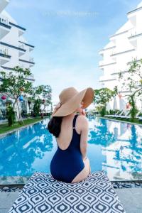 a woman in a hat sitting next to a swimming pool at Gem Riverside Hotel Hoi An in Hoi An