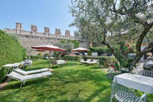 un giardino con tavoli, sedie e un muro di Hotel Villa Cansignorio a Lazise