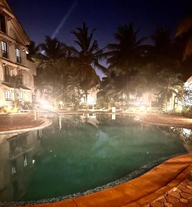 a swimming pool at night with palm trees at Riviera Hermitage in Arpora