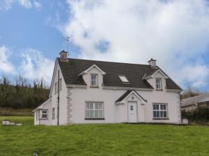 une maison blanche avec un toit noir sur un champ vert dans l'établissement Gunn's Cottage, à Killyhevlin