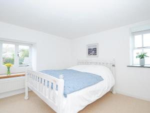 a white bedroom with a white bed and two windows at Cobb Cottage in St Austell