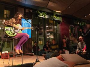 a woman sitting on a chair with a guitar on a stage at 21 House of Stories Navigli in Milan
