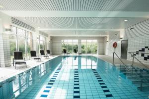 ein großes Schwimmbad mit Stühlen und Tischen in einem Gebäude in der Unterkunft Hotel am Park Bad Driburg in Bad Driburg