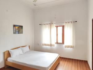 a white bedroom with a bed and two windows at Airport Forest View Ghugugti Farmstay in Dehradun