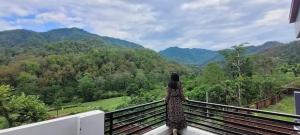 een vrouw op een balkon met uitzicht op de bergen bij Airport Forest View Ghugugti Farmstay in Dehradun