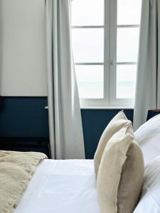 a bed with two pillows in front of a window at Hôtel De La Marine in Arromanches-les-Bains