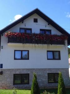 a white house with a balcony with red flowers at Plitvice House Rosha in Plitvička Jezera