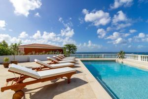 een zwembad met ligstoelen en de oceaan bij Pelikaan Sunset:A Villa With Stunning Ocean Views in Koolbaai