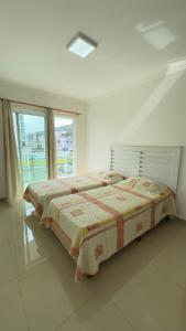 a bed in a white room with a large window at Apto Lírio da Paz- 3 Quartos com sacadas,espaçoso e de frente para avenida principal! in Piratuba +25 photos