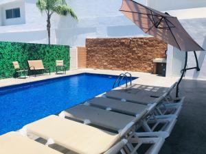 Sleep Inn Mazatlan في مازاتلان: مسبح مع كرسيين للصالة ومظلة