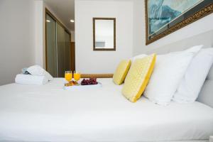 Una cama blanca con almohadas amarillas y dos vasos. en Santino Apartment, en Caniço